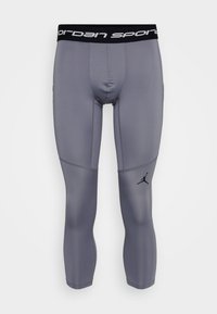 Sivé kompresné legíny s čiernym elastickým pásom, na ktorom je text "Jordan Sport" a malá čierna značka na dolnej ľavej nohe.