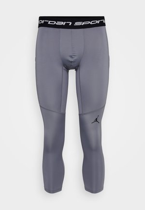 Pelēkas kompresijas legging bikses ar melnu elastīgu jostu, kurā ir "Jordan Sport" teksts un mazs melns logo kreisajā apakšējā kājā.
