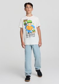 Biała bawełniana koszulka z kolorową grafiką z postacią z kreskówki, w zestawieniu z jasnoniebieskimi dżinsami i czarnymi trampkami.