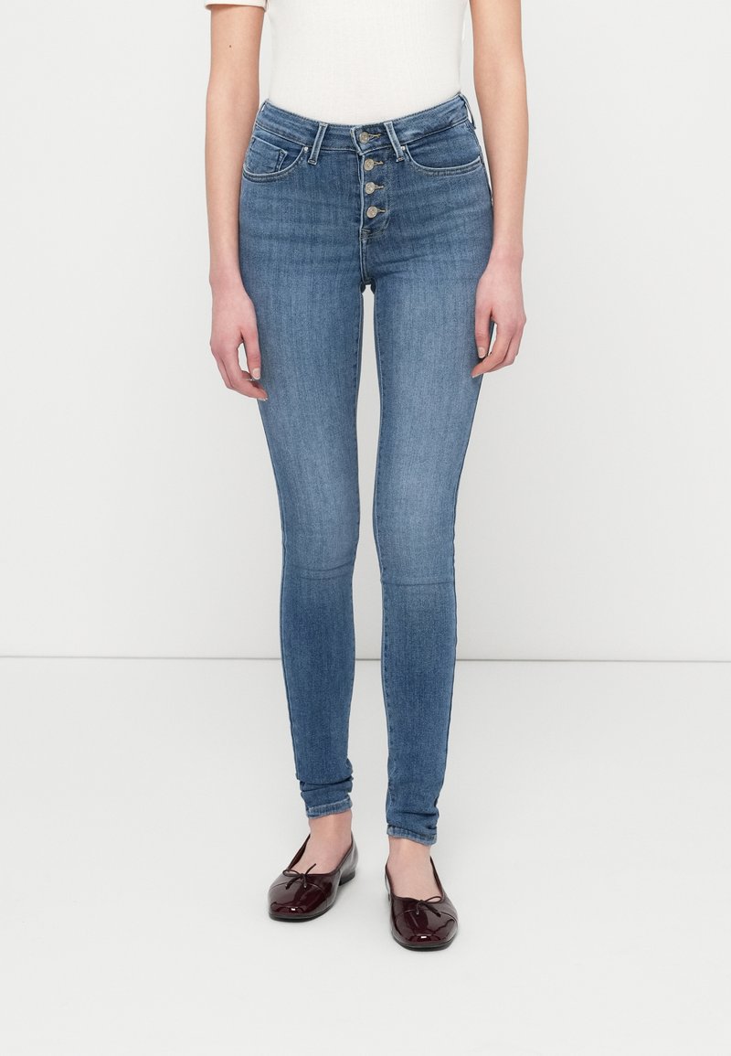 Ψηλόμεσα, ανοιχτού μπλε, στενά τζιν με κλείσιμο με πέντε κουμπιά, δύο μπροστινές τσέπες και ομαλή υφή τζιν.