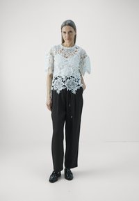 Kanten top met bloemmotieven in lichtblauw, gecombineerd met zwarte, losse broeken en zwarte schoenen. Eenvoudig, elegant ontwerp.