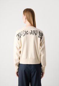 Sudadera de color crema con un corte holgado, que presenta texto negro "MÚSICA. ARTE. AMOR." en la parte posterior y puños y cintura de canalé.