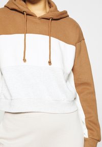Hoodie cropped in blocchi di colore marrone e bianco con cappuccio regolabile e texture morbida. Il design presenta un pannello centrale grigio mélange.