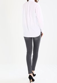 Camisa blanca de botones con mangas largas, combinada con jeans ajustados grises y zapatos de tacón negro. Enfóquese en la textura del tejido y el ajuste.