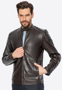 Giacca in pelle marrone con colletto alto, chiusura con zip anteriore e tasche laterali; presenta dettagli a coste sulle spalle e sulle maniche.