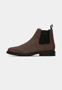 Botte Chelsea en cuir marron avec des panneaux latéraux élastiques, une languette et une surface lisse. Semelle en caoutchouc noir robuste avec un léger talon.