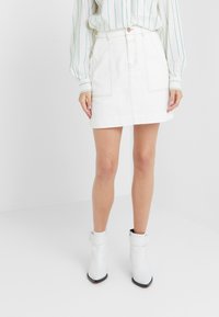 Witte denim rok met twee voorkant zakken, gestikte details en een rechte snit. Gecombineerd met witte enkellaarsjes en een gestreepte blouse.
