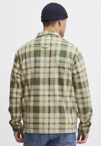 Groene en crèmekleurige geruite flanellen overhemd met blauwe accenten, zachte textuur, kraag, knoopmanchetten en een gebogen zoom, gedragen over een blauwe spijkerbroek.