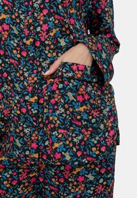 Bluse mit Blumenmuster in Schwarz, mit lebendigen pinken, blauen und orangefarbenen Blumen. Ausgestattet mit einer vorderen Tasche und Knopfverschluss.