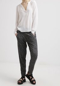 Vit långärmad blus med knappframsidan, matchad med mörkgrå, strukturerade joggingbyxor. Svarta sandaler med tjock sula fulländar looken.