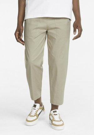 Beiget puuvillahousut rentolla istuvuudella, joissa on sivutaskut ja lyhyt lahkeen pituus, yhdistetty valkoisiin ja beigen sävyisiin urheilutennareihin.