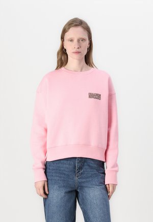 Ροζ κοντό φούτερ με ριμπ φινιρίσματα στα μανίκια και το κάτω μέρος, με μικρό μαύρο εκτύπωμα λογότυπου στο αριστερό στήθος, που φοριέται με μπλε τζιν.