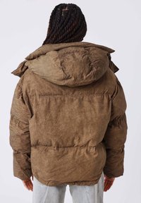 Chaqueta acolchada marrón con acabado texturizado, que presenta una capucha y detalles fruncidos en los hombros y la espalda.