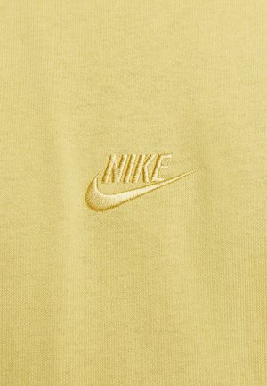 Sárga pamut szövet, hímzett "NIKE" logóval és az azt kísérő sárga swoosh-ral, sima textúrával és minimalista dizájnnal.