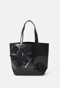 Musta kiiltävä kangaskassi, jossa on suuri nauhadetaili edessä, varustettu kaksoiskahvoilla ja "Ted Baker London" -logolla kultaisena.