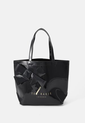 Bolsa de peito preta e espelhada com um grande detalhe em laço na frente, apresentando duas alças e o logótipo "Ted Baker London" em dourado.