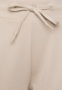Lichtbeige drawstring broeken van een textuurstof, met een bijpassende strik in de taille en kleine metalen accenten aan de uiteinden.
