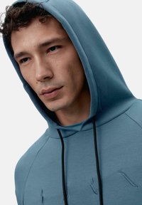 Hooded sweatshirt iz mehke modre bombažne mešanice, z minimalističnim dizajnom, črnim vezalkami in diskretnimi vezeninami.