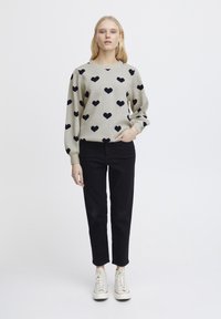 Maglione grigio con motivi a cuore blu navy, scollatura rotonda e maniche lunghe, abbinato a pantaloni neri e sneakers bianche. Design semplice e casual.