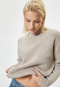 Jasno beżowy sweter z prążkowanego materiału, wykonany z miękkiego materiału, z wysokim dekoltem i luźnym krojem. Wyróżniająca się tekstura i lekko skrócona długość.
