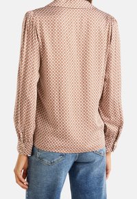 Brun mönstrad blus med långa ärmar, som har en krage och rynkade detaljer. Matchad med ljusblå denimjeans.