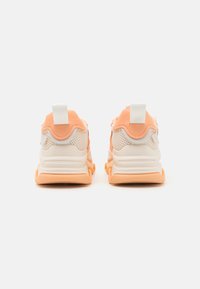 Zapatillas que combinan materiales en naranja claro y blanco, con una parte superior de malla texturizada, suela pronunciada y tiradores en la parte trasera.