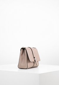 Borsa a mano in pelle beige con pattina texturizzata, bordi neri e chiusura in argento, esposta su un piedistallo bianco contro uno sfondo semplice.