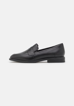 Mocassin noir en cuir à enfiler avec un petit talon, un bout arrondi et une bride décorative sur le dessus, présenté en profil latéral sur fond blanc.