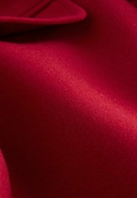 Roter Wollstoff, strukturierte Oberfläche mit glatter Haptik, mit einem gefalteten Rand und subtiler Glanz. Gleichmäßige Farbe, ohne Muster oder Akzente.