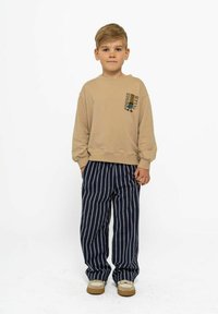Beige sweatshirt met "Foodie Club" graphic, gecombineerd met marineblauwe gestreepte broek. Schoenen zijn beige met witte accenten. Heldere, minimalistische uitstraling.