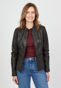 Sort læderjakke med lynlås, rund krave og vertikale syninger. Båret med en maroon top og højtaljede blå jeans.