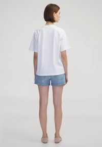 Witte short-sleeve shirt met een rechte zoom, gecombineerd met lichtblauwe denim shorts. De outfit wordt aangevuld met beigerkleurige platte schoenen.