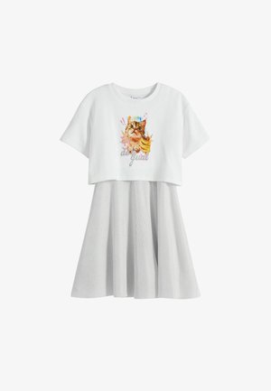 Valkoinen lyhythihainen paita, jossa on kissagrafiikka, vaaleanharmaan tekstuurilla varustetun hameen päällä. Hameessa on poimutuksia ja liehuva muoto.