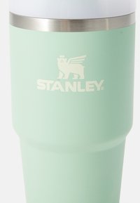 Stanley travel mug in soft mint green with a matte finish, stainless steel accent, and embossed logo featuring a lion and crown design.