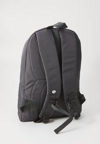 Sac à dos en tissu noir avec des bretelles réglables, un panneau arrière rembourré et un accent de logo. Comprend un tressage pour un maintien supplémentaire.