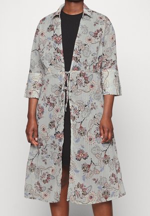 Frau trägt einen hellgrauen, floralen Kimono-Morgenmantel mit 3/4-Ärmeln, in der Taille gebunden, über einem schwarzen, gerippten Kleid.