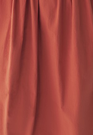Jupe de couleur rouille en tissu léger avec une texture lisse, présentant de doux plis qui créent du volume et un drapé.