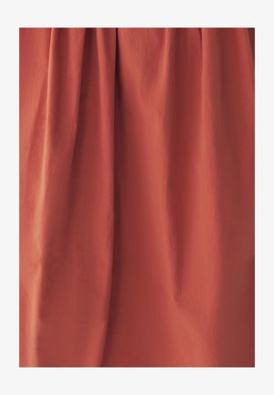 Jupe de couleur rouille en tissu léger avec une texture lisse, présentant de doux plis qui créent du volume et un drapé.