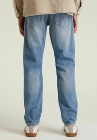 Jeans de mezclilla azul claro con un diseño de pierna recta, que cuentan con dos bolsillos traseros y un acabado desgastado. Llevados con zapatos blancos y grises.