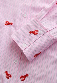 Pink striped shirt featuring embroidered red lobsters. Cotton material with white buttons, fine horizontal lines, and a smooth texture.