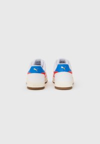 Sneakers bianchi con accenti rossi e blu, dotati di una tomaia testurizzata, punta rotonda e suola in gomma beige. Dettaglio del logo dorato sul tallone.