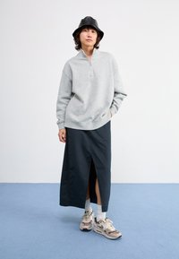 Šviesiai pilkas užtrauktuku užsegamas megztinis su bobroviniu apvadu, derinamas su tamsiai mėlynomis, iki kulkšnies ilgio sijonais su šoniniu plyšiu. Dėvimi su smėlio spalvos sportbačiais.