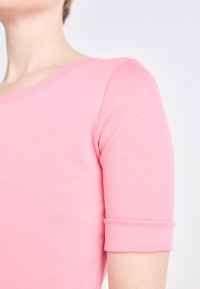 Aangesloten roze katoenen top met een ronde hals en korte opgerolde mouwen, met een gladde textuur en minimale stikdetails.