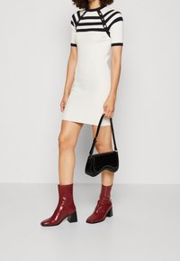 Robe en maille crème à rayures bleu marine avec des boutons en accent ; assortie d'un sac à main noir et de bottines brillantes bordeaux à talons blocs.