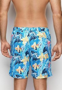 Bañador azul con un patrón vibrante de orquídeas amarillas y hojas verdes, con una cinturilla elástica y un bolsillo lateral.