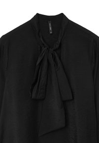Blouse noire en tissu texturé, avec un col à lacer. Elle a une coupe décontractée et un col simple, adaptée à diverses occasions.