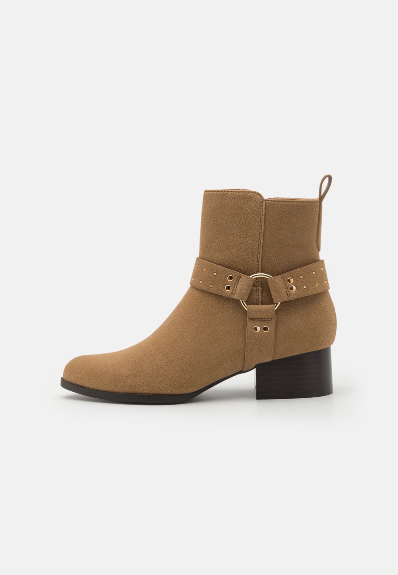 Botas de tobillo de ante marrón con punta redondeada, tacón plano y una correa decorativa que presenta herrajes circulares y pequeñas tachuelas.