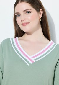 Grünes V-Ausschnitt-Oberteil mit einem Kragen aus drei Streifen in Weiß, Pink und Mintgrün. Glatter Stoff mit einem entspannten Schnitt.