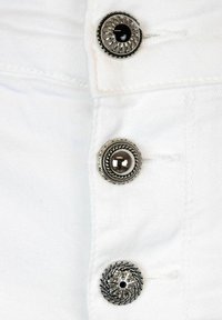 Tessuto di denim bianco con tre bottoni argentati, caratterizzato da motivi testurizzati e un centro nero lucido. Sono visibili dettagli cuciti nelle vicinanze.