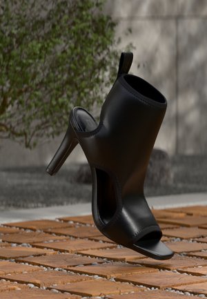Scarpa mule nera con tacco alto, punta aperta e lati ritagliati, mostrata all'aperto su listelli di legno con sfondo di fogliame verde sfocato.
